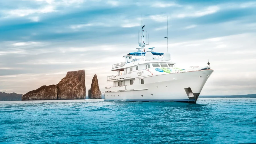 Luxury yacht cruising near dramatic rock formations under a serene sky.