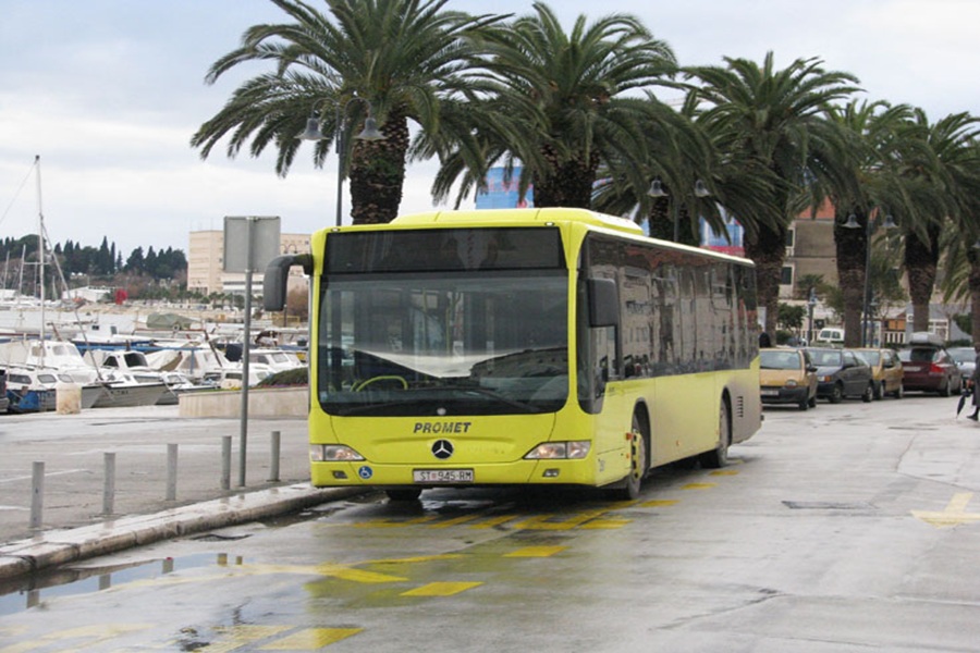 Yellow city bus at waterfront in Split with palm trees and marina background.