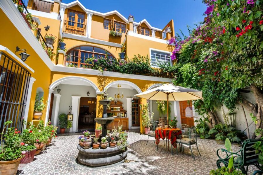 Colorful boutique hotel courtyard with yellow walls, tiered fountain, lush plants, and outdoor dining.