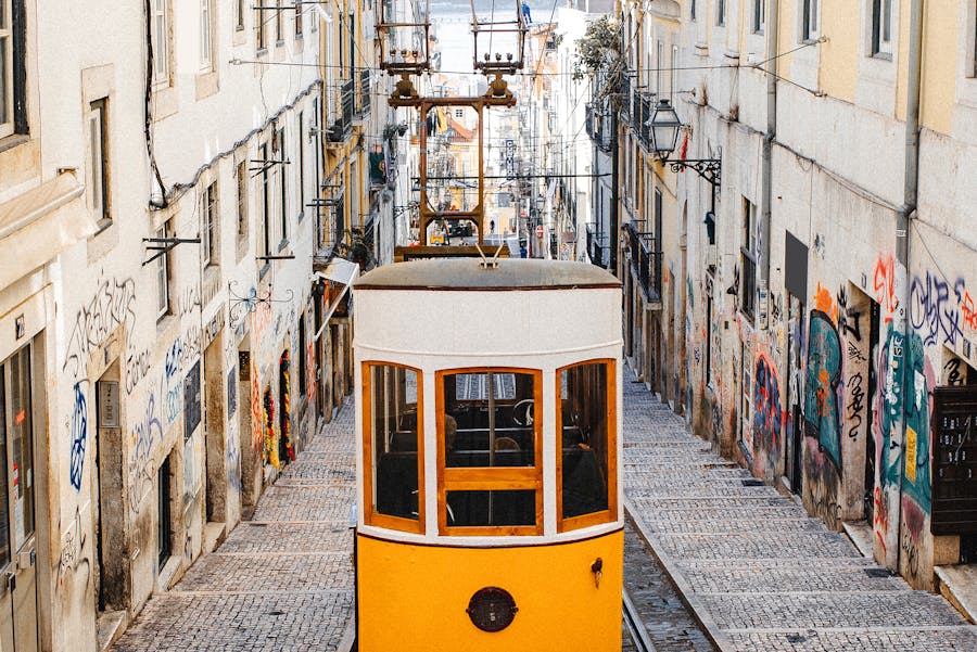 Yellow vintage tram on steep cobblestone street in historic urban neighborhood.
