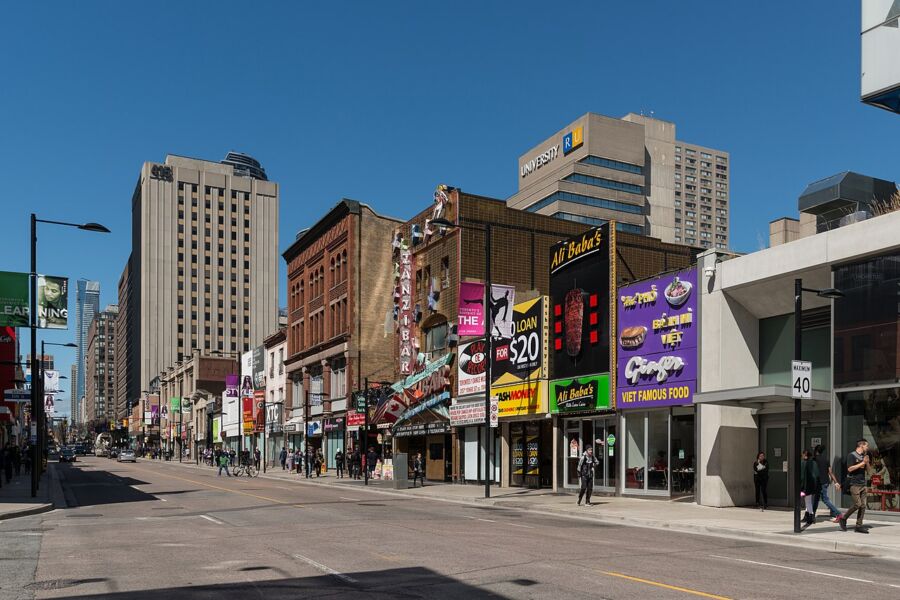 Bustling Yonge St in Toronto, featuring numerous buildings and pedestrians walking along the busy city street.