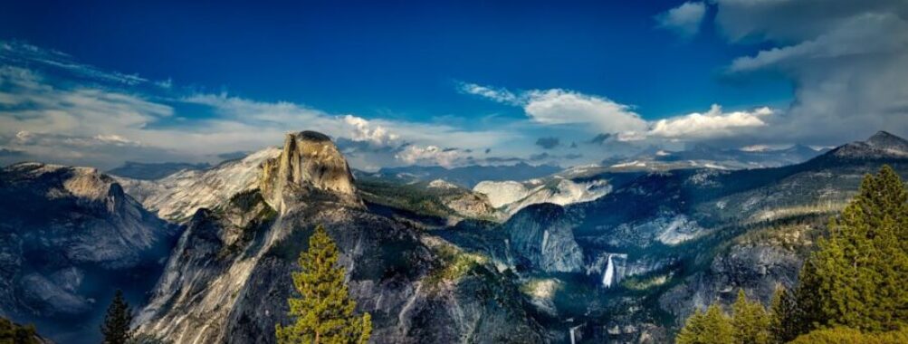 Half Dome in Yosemite: majestic granite, lush forests, dramatic clouds, waterfall backdrop.