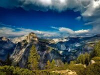 Half Dome in Yosemite: majestic granite, lush forests, dramatic clouds, waterfall backdrop.