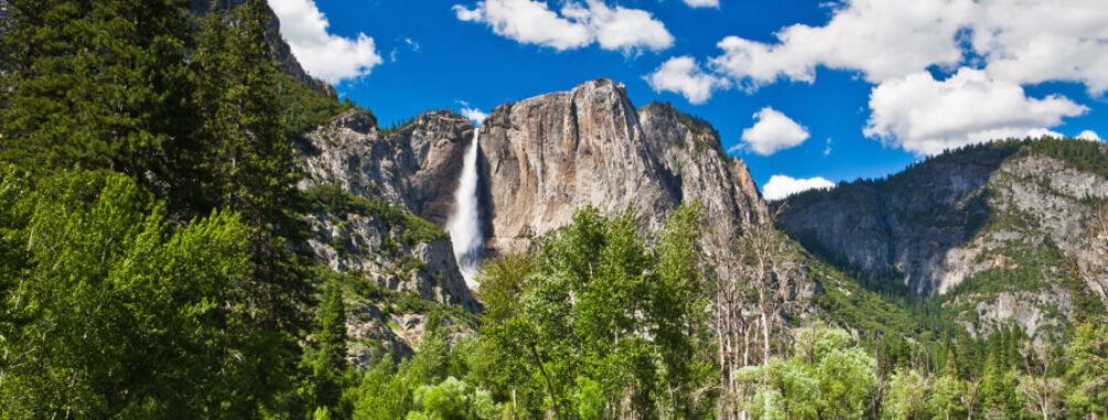 The sun sets behind Yosemite's majestic cliffs, illuminating the sky with shades of orange and pink in a tranquil scene.