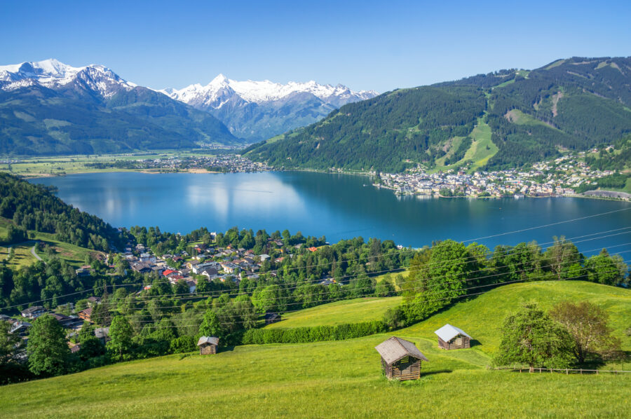 Scenic view of Zell am See, showcasing snow-capped mountains, lush green valleys, and a serene lake under a clear blue sky