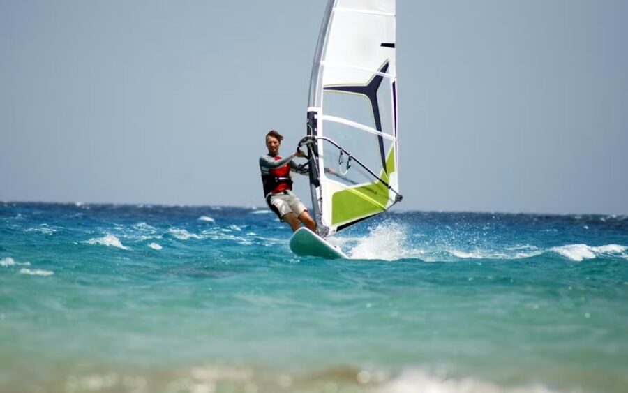 Man skillfully windsurfing in the ocean, participating in a trial course at Zingst, with a clear blue sky above.