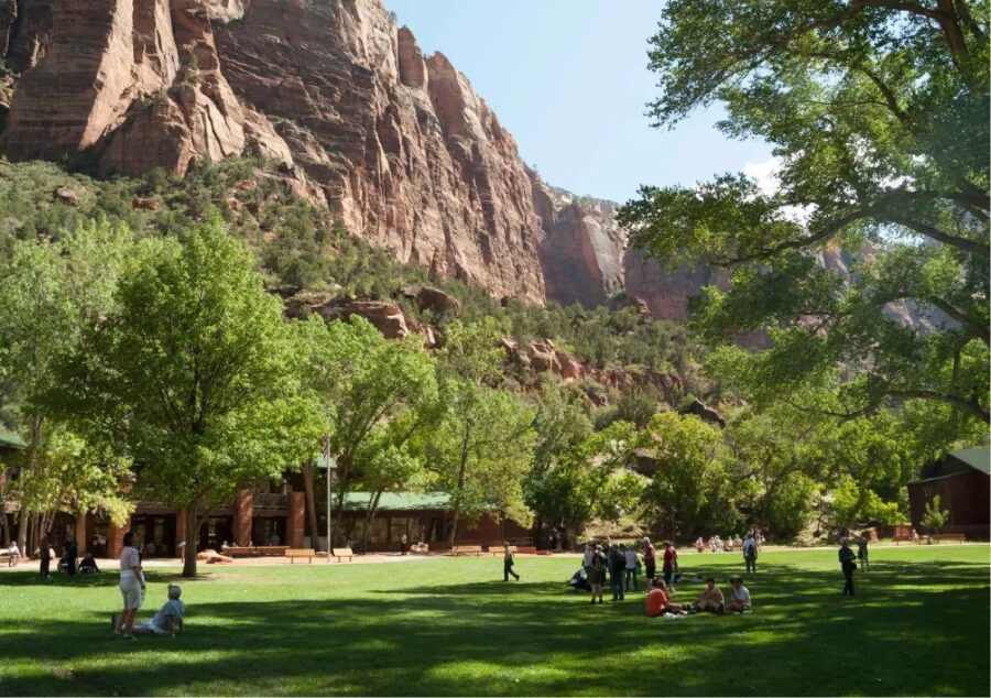 People relax on the grass in front of a mountain near Zion National Park Lodge, enjoying the scenic landscape.
