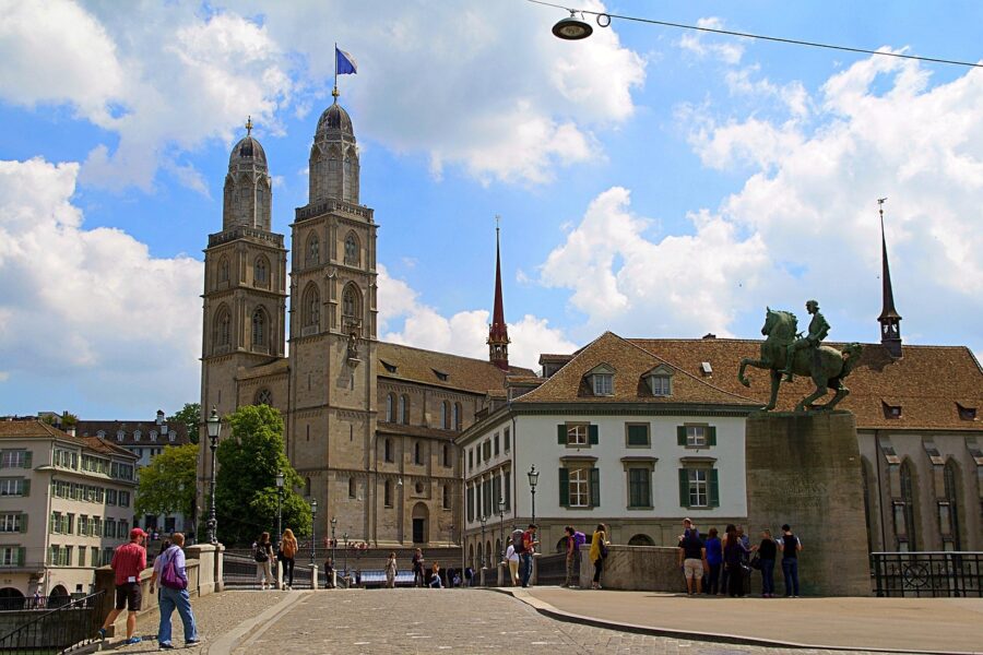Zurich cityscape featuring Grossmünster church, stone bridge, historical architecture, and vibrant urban life.