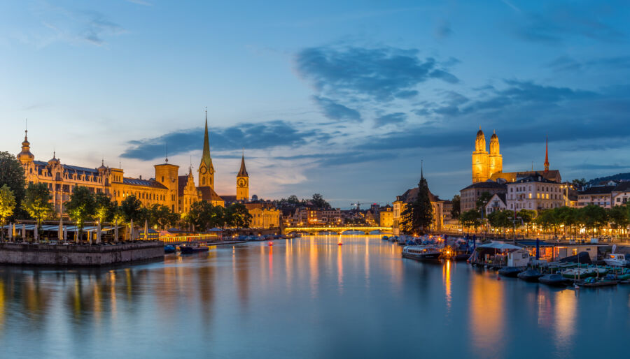 Night view of Zurich's skyline featuring Fraumünster and Grossmünster churches by Lake Zurich, illuminated against the dark sky.