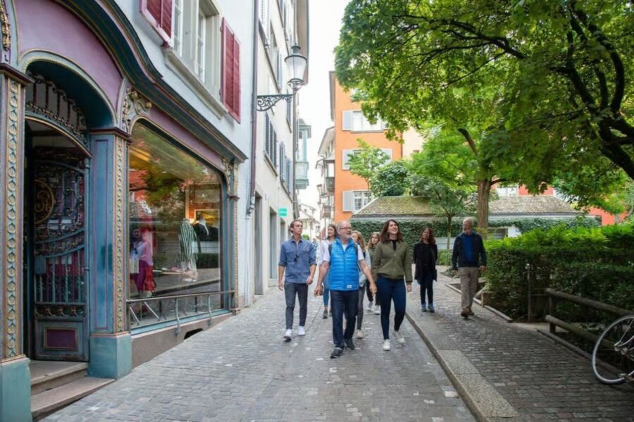 Group of people strolls along a cobblestone street during a Zurich walking tour experience.